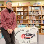 Rachel Kresl leans against a desk in a library with a banner that has text 