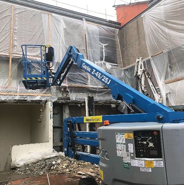 a lift truck in front of a 2-story building that is covered in plastic film