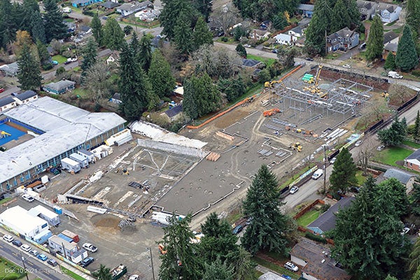 aerial view of a construction site with steel framing on right side and an existing building on left side