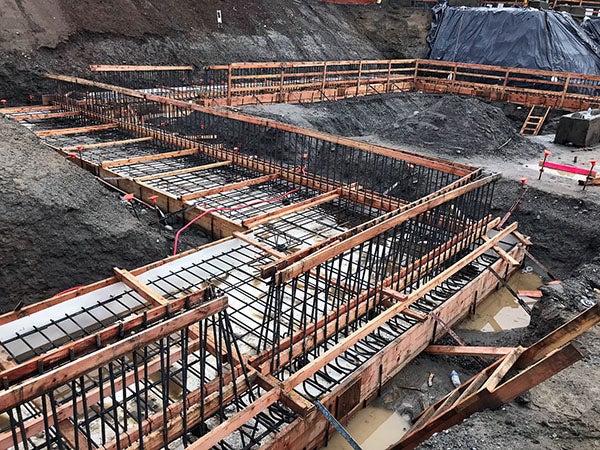a construction site has steep soil walls and a zig-zag of concrete forms with rebar at the bottom and up the sides