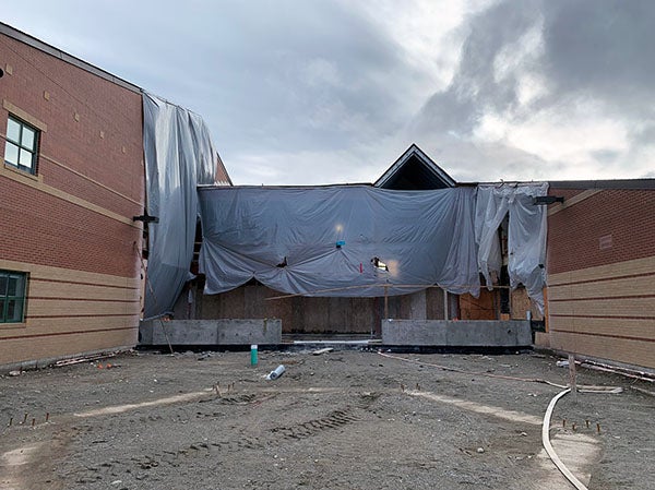 two wings of a brick building have a section between them that is under construction with plastic sheeting partially covering it