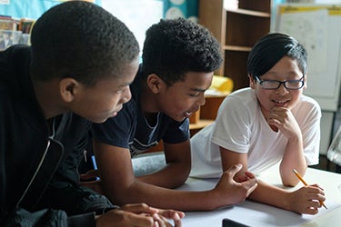 Three middle school students talk together in a classroom.