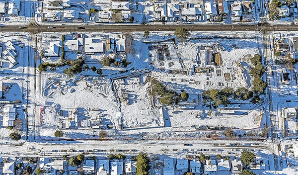 an aerial view of a construction site covered in snow with a cleared street above it and snowy streets around it