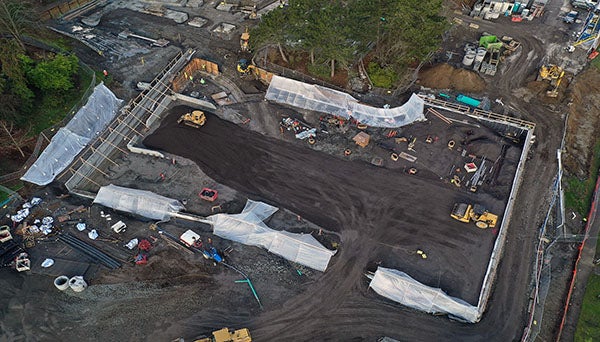 aerial view of constrution site with open dirt area and equipment and concrete forms covered in clear materials on the edges