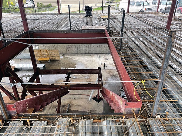 a framed floor with a grid on it has a hole in that has two edges for a stairway going down