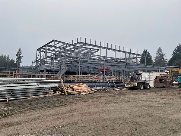 structural steel frame for large building with dirt, materials, and equipment in front