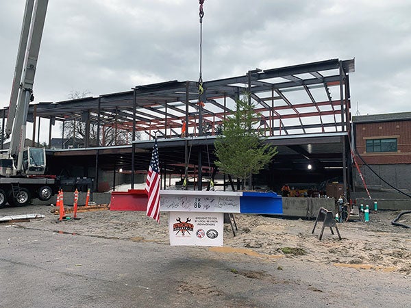 final structural steel beam is painted red, white, and blue; has signatures on the white part; has flag and evergreen tree attached