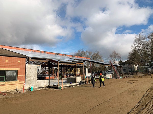 a steel framed building under construction is attached to an existing brick building at one end