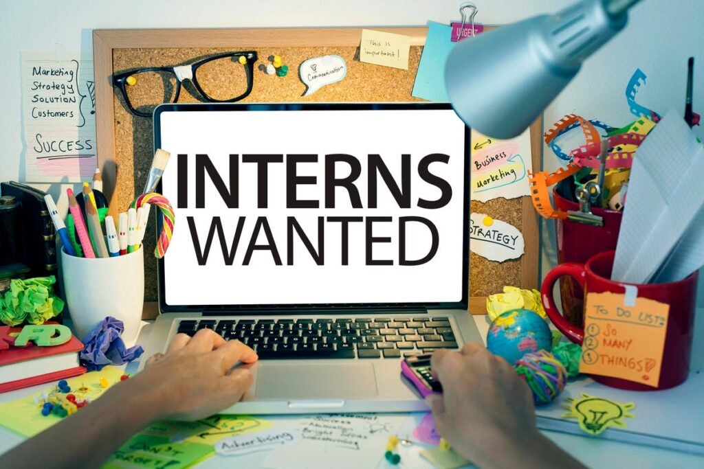 An illustration of a person using a laptop with screen that says "Interns Wanted"