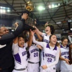 A girls basketball team and coach cheer on the court at they hold a trophy