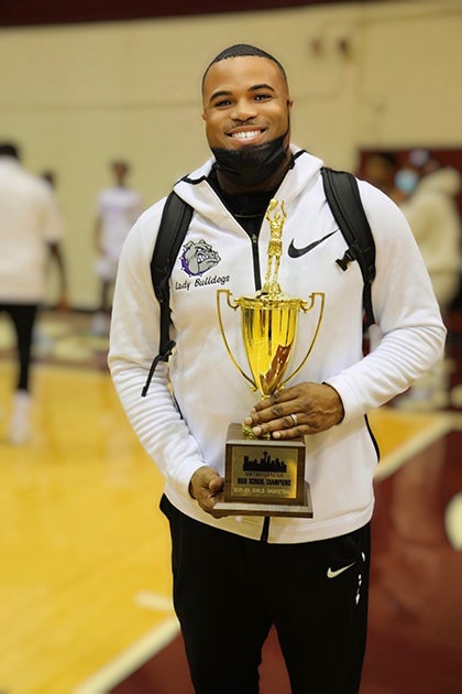 A coach holds a trophy on a court and smiles for a photo