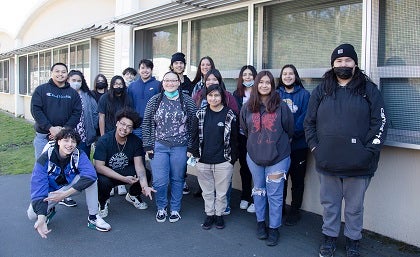 A group of students pose for a photo outside a classroom.