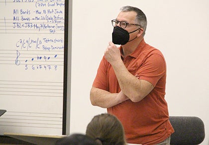 Scott Brown holds his hand to his chin while listening to students in a music classroom.