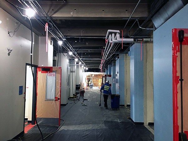 a hallway with doors. the floor is covered with protective material and the ceiling has been removed so you can see wires and beams