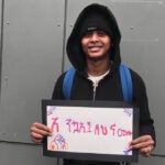 A student smiles for a photo with a sign that says welcome in Amharic
