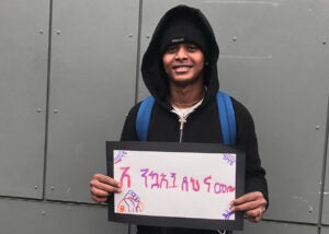 A student smiles for a photo with a sign that says welcome in Amharic