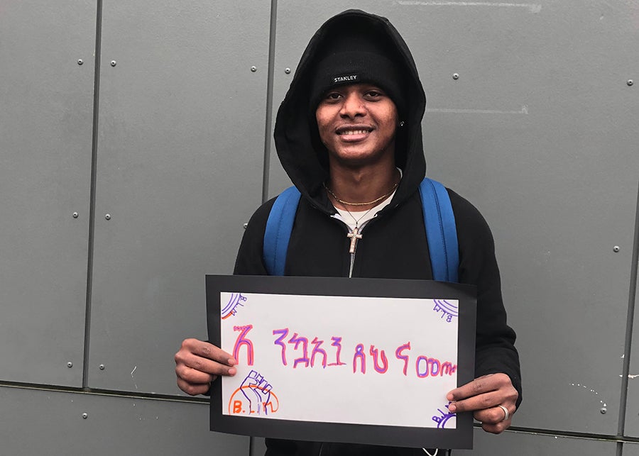 A student smiles for a photo with a sign that says welcome in Amharic