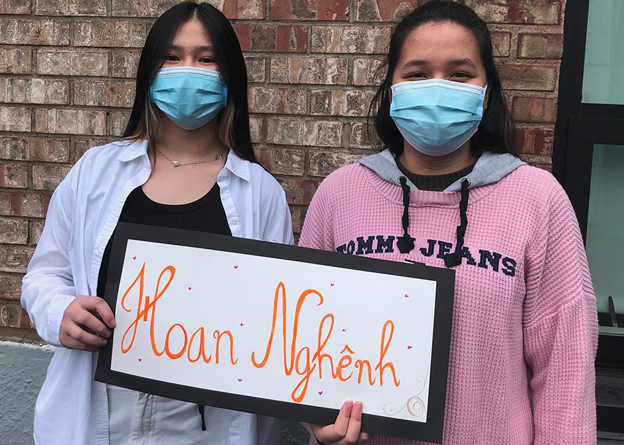 Two students in masks hold a sign that says welcome in vietnamese