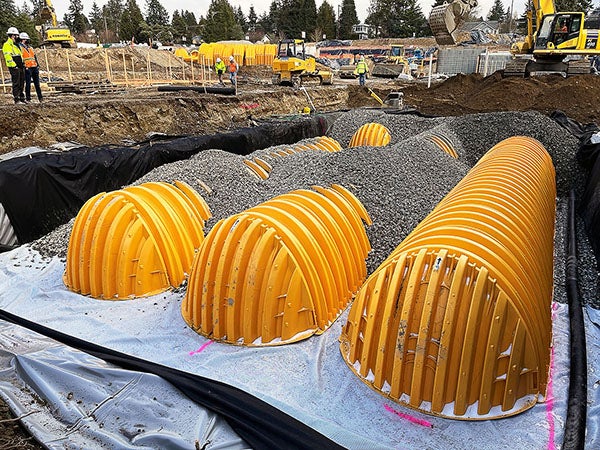 a large hole at a construction site has material under yellow curved pieces that are partially covered with gravel