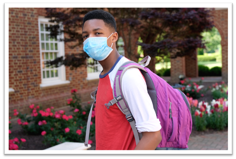 A student with a mask stands in front of a school