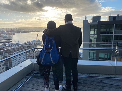 A student and adult stand watching the sunset on top of a building in downtown Seattle.