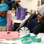 A parent watches a student as she works on a project in a classroom