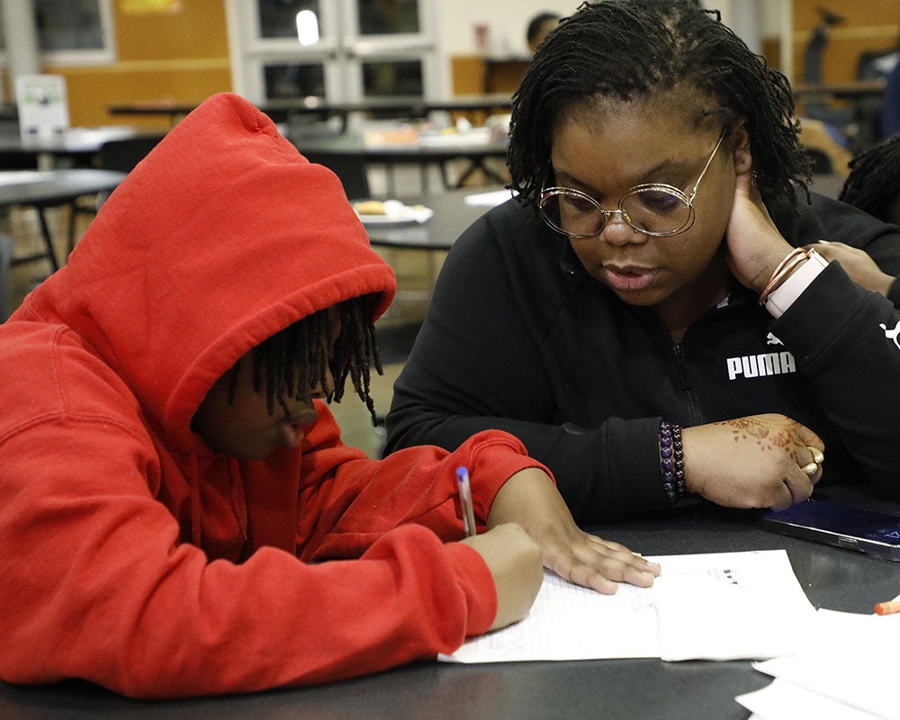 A parent watches as a student works on a project in a classroom