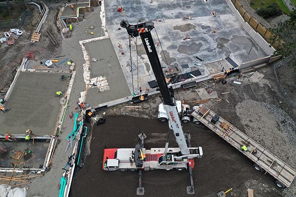 aerial view of a crane with workers attaching a piece of structural steel
