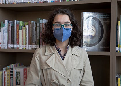 A high school student stands in front of a library shelf with a health safety mask on.