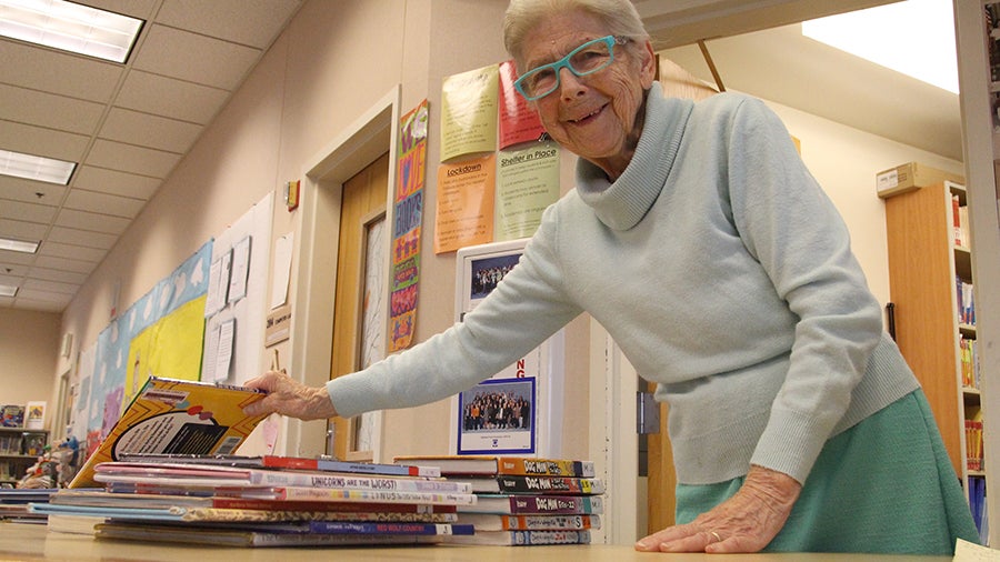 A school library volunteer stands at a table with several elementary age books
