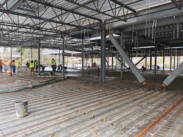 workers in a steel structure with a metal roof are working on concrete that is being poured