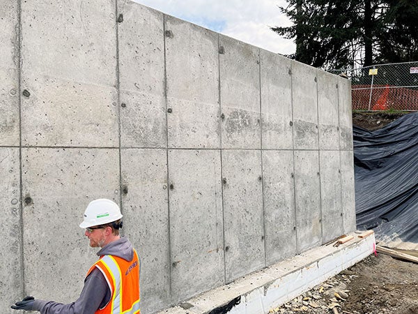 a very tall concrete wall with a person standing in front of it. the person comes up about 1/3 of the height