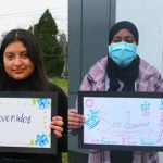 A group of students pose with a hand drawn sign that says welcome in different languages