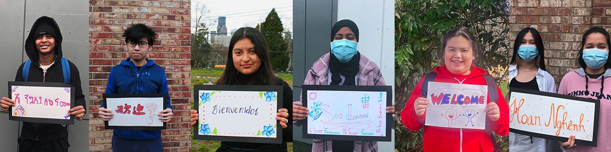 Several students stand with hand drawn signs that say Welcome in different languages.
