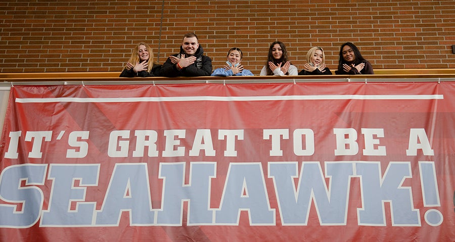 Six high school students form a bird with their hands while standing next to a sign that says 'It's great to be a seahawk!"