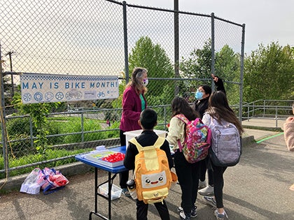 An adult talks with four students in front of a table with treats and information about biking