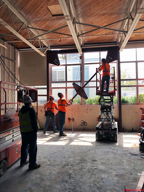 workers are lifting steel into place in front of windows