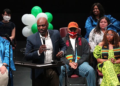 Superintendent Jones speaks at a podium with graduates behind him during a graduation ceremony