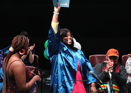 A graduate holds up her certificate while standing on a stage during a graduation ceremony