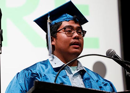 A graduate in cap and gown stands at a podium during a graduation ceremony