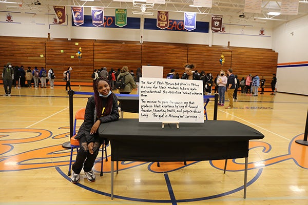 Black Student Union Organizer smiles at the camera while sitting posed next to a poster board with inspiring words on it.