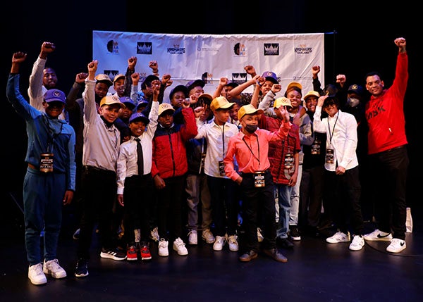 A group of students and mentors gather for a photo on a stage.