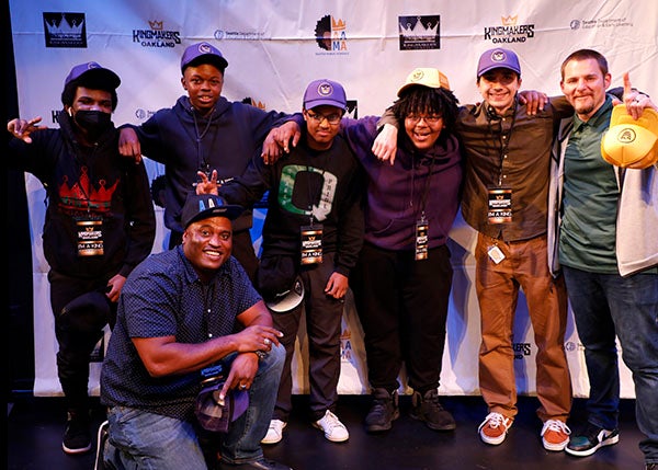 A group of students and mentors gather for a photo on a stage.