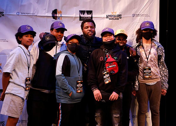 A group of students and mentors gather for a photo on a stage.