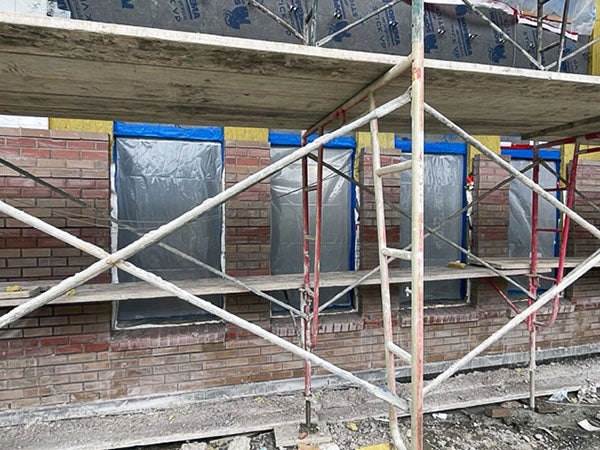 a scaffolding in front of windows with brick partially around them