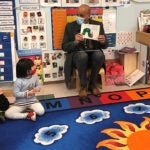 A classroom of preschool students listen to an adult read a book