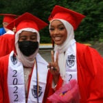 Two graduates smile for a photo in cap and gown.
