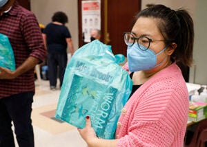 A woman holds up a bag of books for students to select in a school auditorium 