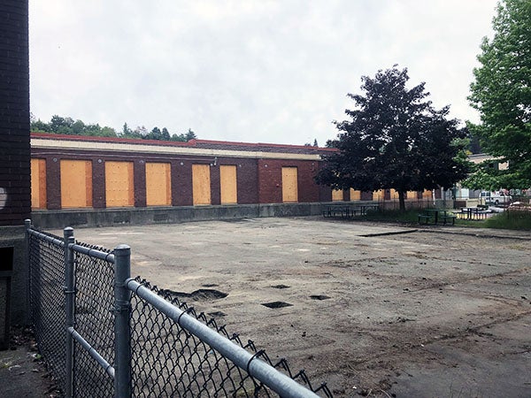 a concrete area in front of a brick building with boarded up windows