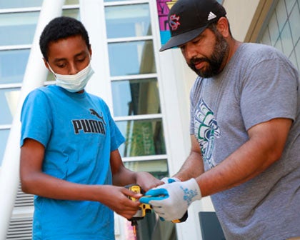 A teacher and student work together on a construction project outside a school